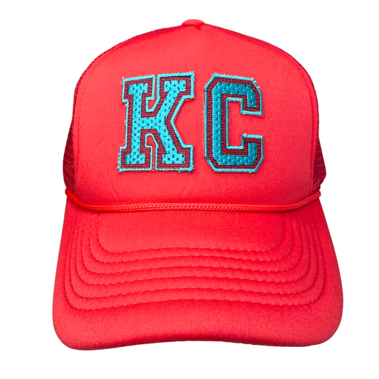 Front view of red trucker hat with teal and black KC patch in Kansas City Current colors

