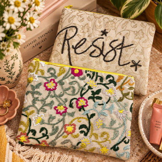 Hand-embroidered Resist clutch showing both floral and Resist sides in a warm styled flat lay