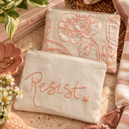 Hand-embroidered Resist zipper clutch showing both peach embroidered sides in a warm styled flat lay