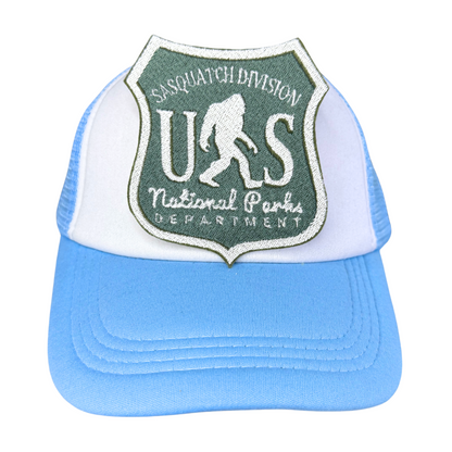 "Blue and white trucker hat featuring an embroidered Sasquatch Division National Parks patch in forest green and white."
