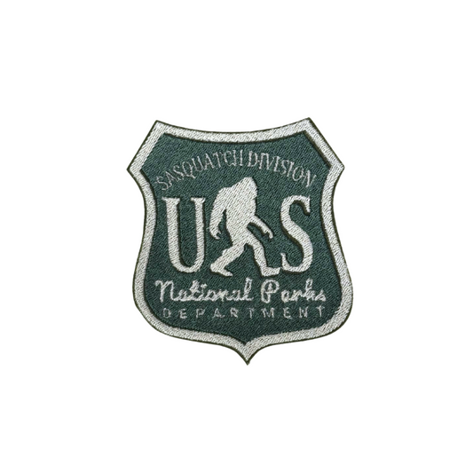 "Embroidered patch in the shape of a National Parks badge with a green and white design featuring Bigfoot and the words 'Sasquatch Division' and 'National Parks Department.'"
