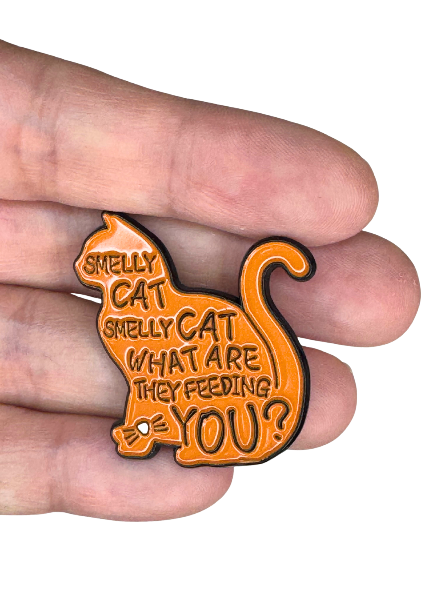 Smelly Cat enamel pin held between fingers for size

