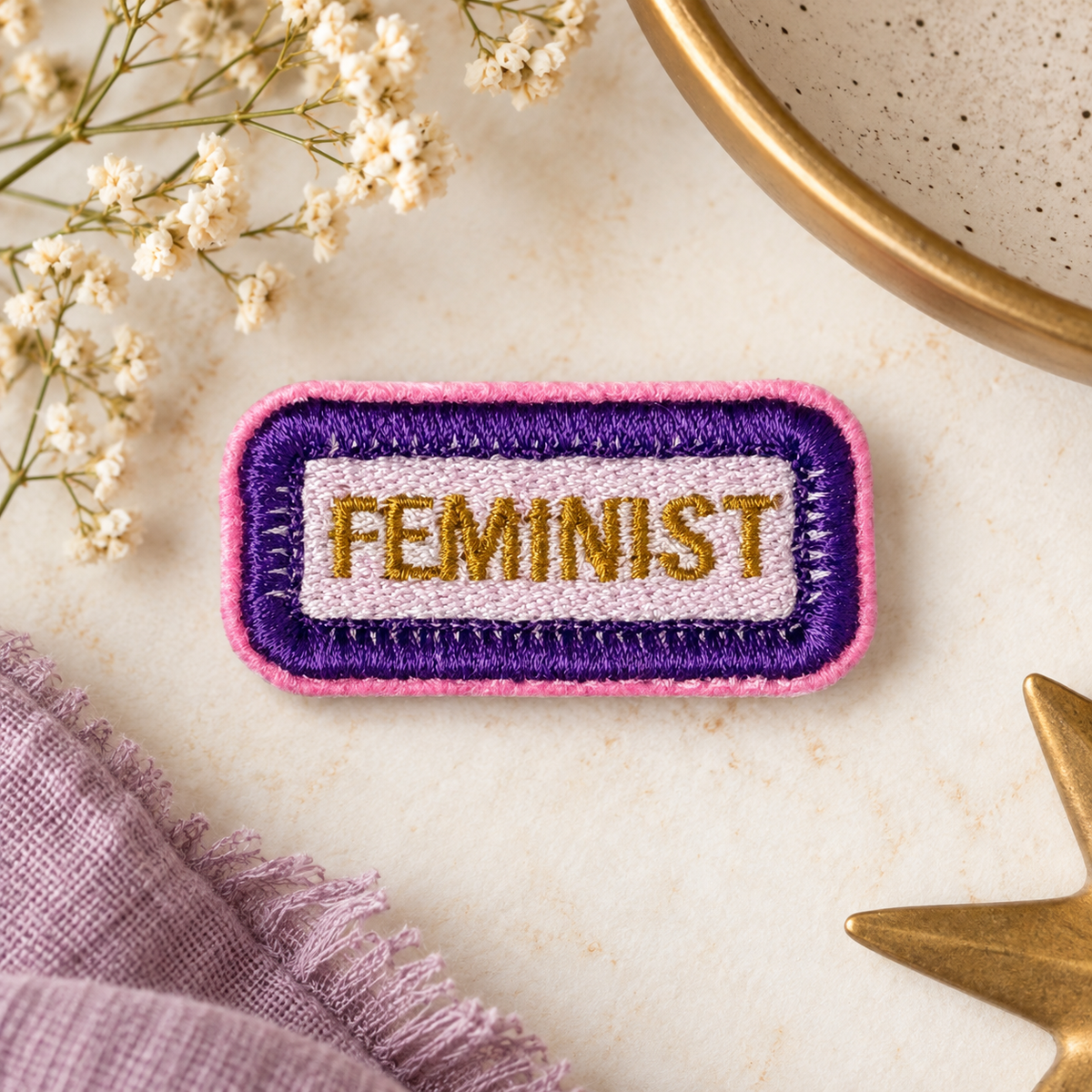 FEMINIST embroidered patch in purple, pink and gold on warm styled flat lay with flowers