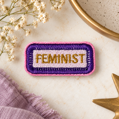 FEMINIST embroidered patch in purple, pink and gold on warm styled flat lay with flowers