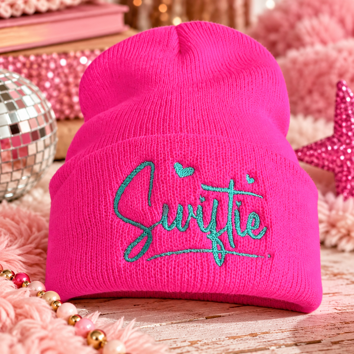 Hot pink Swiftie embroidered beanie with teal script in a bright styled scene