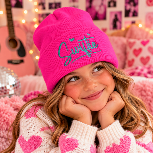 Youth wearing hot pink Swiftie embroidered beanie with teal script in a playful pink room