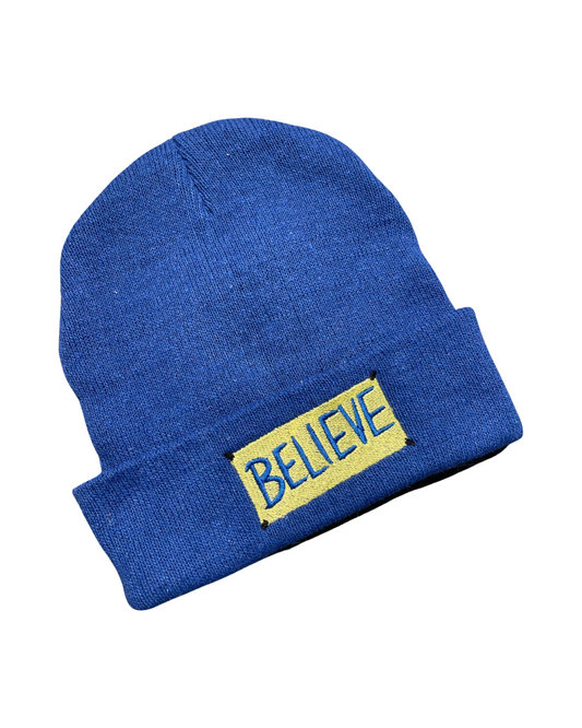 royal blue knit beanie embroidered with the "BELIEVE" sign from Ted Lasso