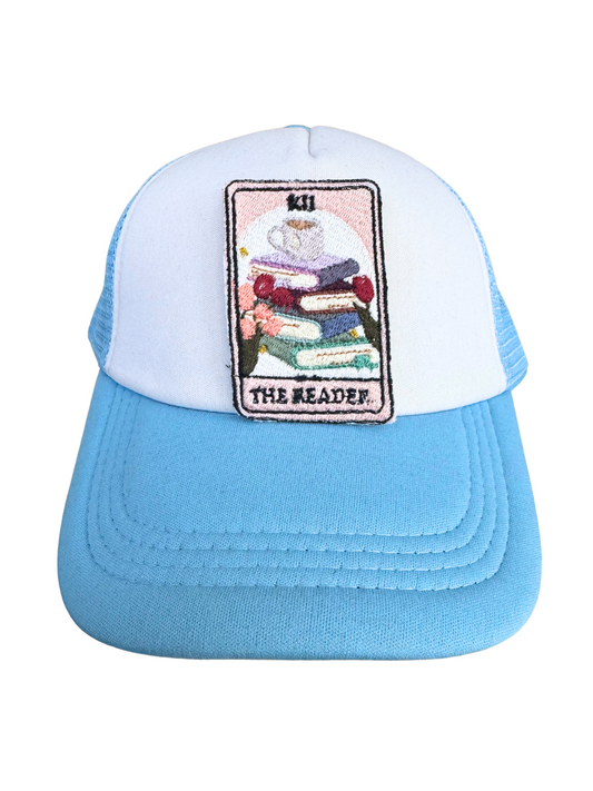 Blue and white trucker hat styled with "The Reader" embroidered patch, ideal for book lovers and cozy aesthetic fans.
