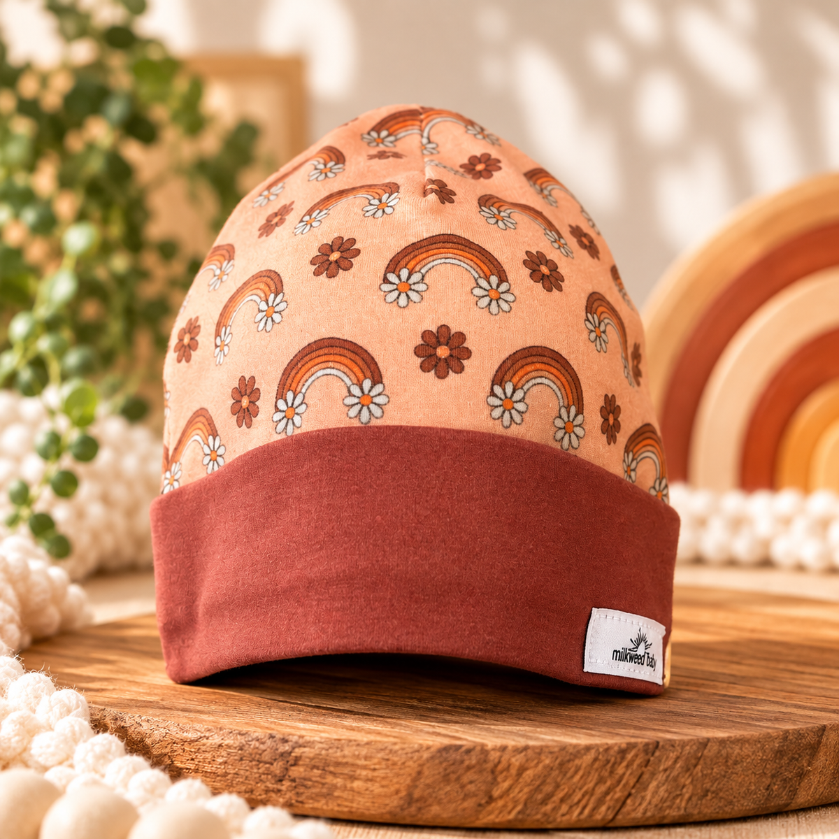 Vintage rainbow and daisy organic cotton baby beanie with rust cuff styled on warm wooden surface