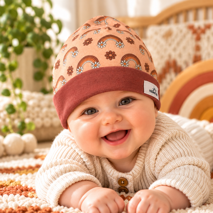Baby wearing peach vintage rainbow and flower beanie with rust cuff in a cozy nursery