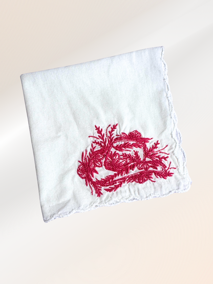 A folded embroidered handkerchief showcasing a floral cowboy hat design stitched in red on soft white fabric, handmade in Kansas City.

