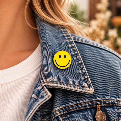 One-inch yellow smiley face enamel pin worn on the collar of a blue denim jacket