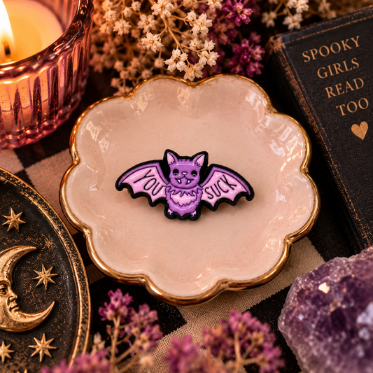 You Suck vampire bat enamel pin styled in a warm spooky Milkweed Baby flat lay